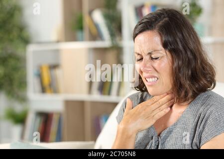 Femme adulte en douleur souffrant de mal de gorge assise dans le canapé à la maison Banque D'Images