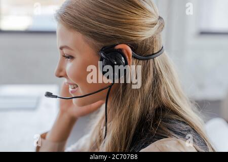 vue latérale d'un opérateur joyeux dans un casque souriant au bureau Banque D'Images