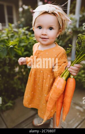 Fille enfant dans le jardin tenant des carottes saine alimentation végétalienne manger mode de vie légumes biologiques produit maison cru agriculture locale concept Banque D'Images