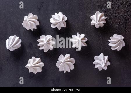 Motif avec dix biscuits meringue blancs sur la surface de table en pierre texturée noire. Arrière-plan doux, plat, directement au-dessus de la vue. Concept alimentaire malsain Banque D'Images