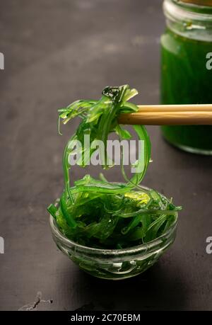 Sélection sélective, salade de Chuka de mer aux graines de sésame dans des plats en céramique blanche, avec des bâtonnets de bambou sur fond sombre Banque D'Images