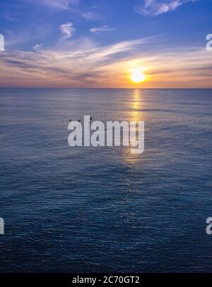 Un groupe de quatre pélicans survole les vagues de l'océan tandis que le soleil émet un faisceau à travers l'eau pendant le lever du soleil à Carolina Beach, Caroline du Nord, États-Unis Banque D'Images