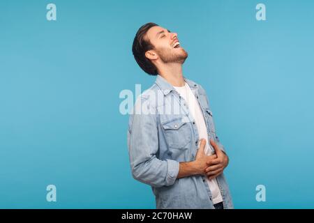 Portrait d'un homme insouciant heureux dans une chemise en denim ouvrier riant à voix haute et tenant le ventre, chassant étant hystérique à la plaisanterie drôle, anecdote hilarante Banque D'Images