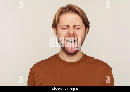 Portrait d'un drôle d'homme optimiste avec barbe portant un sweat-shirt se comportant naughty puéril, montrant la langue dehors et faisant des visages, désobéissant goofy grima Banque D'Images