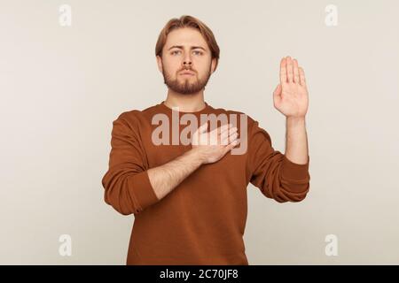 Je promets de dire la vérité! Portrait de l'homme barbu honnête responsable en sweat-shirt debout levant la main et de dire jurer, faisant serment de loyauté, pledgin Banque D'Images