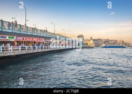 Les gens dînant, marchant et pêchant le long du pont de Galata à Istanbul, en Turquie, tandis qu'un ferry s'approche sur le détroit du Bosphore. Banque D'Images