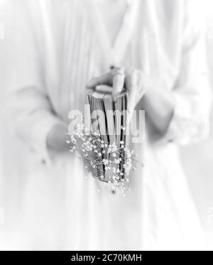 Une jeune femme tenant un livre ancien avec des fleurs blanches sur fond blanc, photographie en noir et blanc, photographie de la vie encore, gros plan Banque D'Images