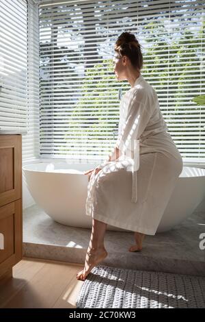 Femme en peignoir assise sur la baignoire Banque D'Images