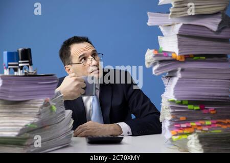 Un employé de bureau regarde avec surprise les énormes papiers de pile sur le bureau devant lui Banque D'Images