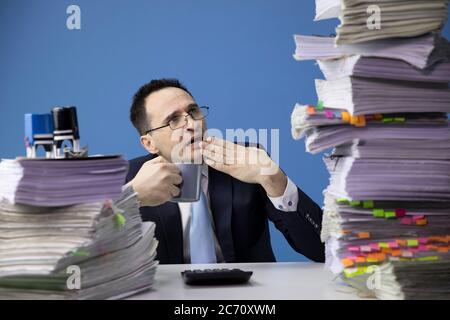 Le préposé au bureau est surpris par les énormes papiers de pile sur le bureau et bât Banque D'Images