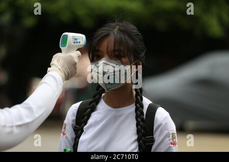 Yangon, Myanmar. 13 juillet 2020. Un membre du personnel mesure la température d'un étudiant à la porte d'une école pendant la journée d'inscription à Yangon, au Myanmar, le 13 juillet 2020. Le Myanmar a lancé mardi les inscriptions à l'école pour l'année scolaire 2020-2021, qui a été retardée en raison de la pandémie COVID-19. Crédit: U Aung/Xinhua/Alay Live News Banque D'Images