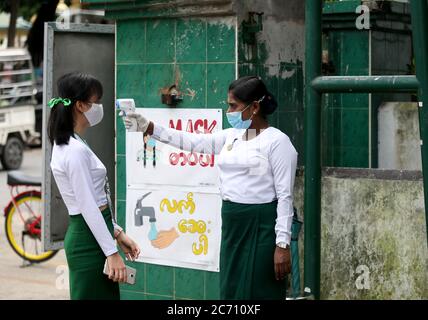 Yangon, Myanmar. 13 juillet 2020. Un enseignant portant un masque mesure la température d'un étudiant à la porte d'une école pendant le jour de l'inscription à l'école à Yangon, Myanmar, le 13 juillet 2020. Le Myanmar a lancé mardi les inscriptions à l'école pour l'année scolaire 2020-2021, qui a été retardée en raison de la pandémie COVID-19. Crédit: U Aung/Xinhua/Alay Live News Banque D'Images