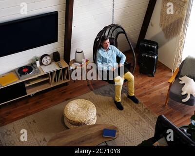 Un homme s'assoit dans une chaise à la maison et travaille à un ordinateur portable. Intérieur moderne et travail à distance. Banque D'Images