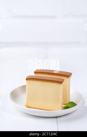 Castella (kasutera) - magnifique délicieux gâteau japonais tranché plat blanc sur table rustique en bois blanc, gros plan, copie design d'espace Banque D'Images