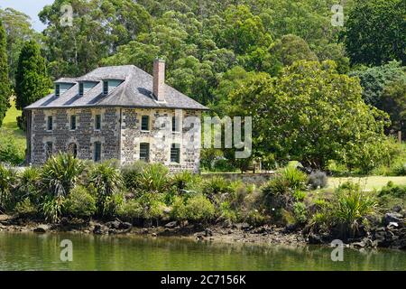 Maison en pierre de la Mission historique à Kerikeri entourée d'arbres et de plantes vertes - lac et rive en face Banque D'Images