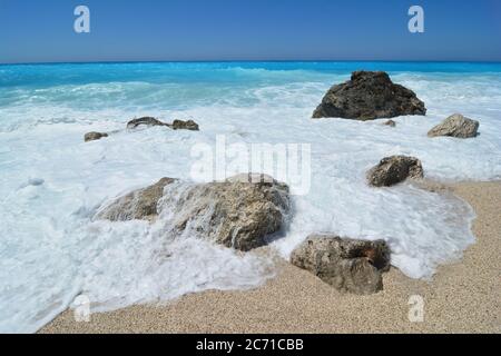 Petit groupe de pierres en galets, recouvert de mousse de mer et de vagues d'eau turquoise dans un lumineux, ensoleillé jour après la tempête, plage Kathisma, île Lefkada, Banque D'Images