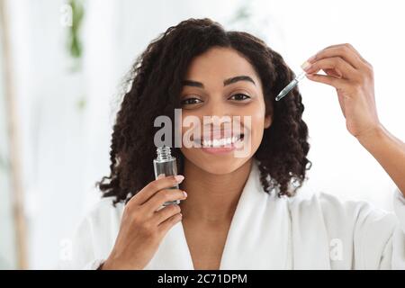 Produits de soins pour la peau. Femme africaine souriante tenant une bouteille avec un sérum hydratant pour le visage Banque D'Images