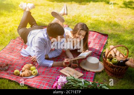 Couple heureux mariés lisant le livre ensemble pendant le pique-nique dans la campagne Banque D'Images