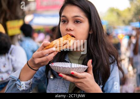 Une fille mangeant de la pâte feuilletée de pommes de terre (patties Aloo) au marché extérieur de la rue à l'heure du jour. Lieu de tournage Sarojini Nagar, Delhi, Inde. Banque D'Images