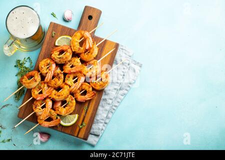 Brochettes de crevettes grillées ou langoustines servies avec de la chaux, de l'ail et de la sauce sur fond de béton bleu clair. Fruits de mer et bière. Vue de dessus avec copie Banque D'Images