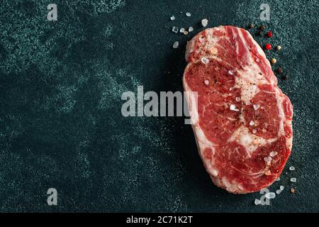 Viande fraîche crue Ribeye Steak et assaisonnement sur fond sombre. Vue de dessus avec espace de copie. Pose à plat Banque D'Images