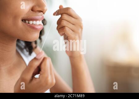 Entretien des dents. Femme noire souriante avec des dents parfaites utilisant la soie dentaire Banque D'Images