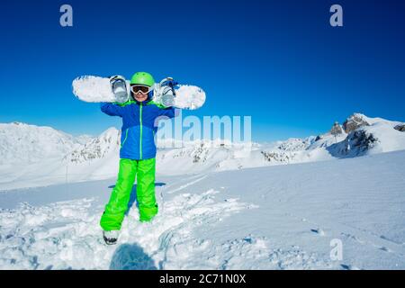 Portrait en hauteur d'un garçon tenir le snowboard sur les épaules se tenir dans la neige sur la montagne vue de haut de gamme sur l'arrière-plan Banque D'Images