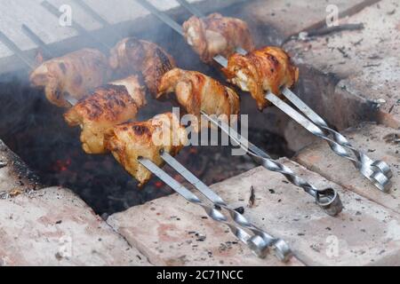 Gros plan des cuisses de poulet accrochées sur des brochettes et frites sur un feu ouvert, foyer sélectif Banque D'Images