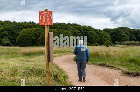 East Lothian, Écosse, Royaume-Uni, 13 juillet 2020. Météo au Royaume-Uni : couvert à la plage de Yellowcraig. Des mesures de distanciation sociale sont en place sur le trajet entre le parc automobile et la plage, tandis qu'un homme senior marche le long du sentier pendant la pandémie du coronavirus Covid-19 avec un avis de rester à 2 mètres d'écart Banque D'Images