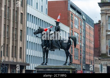 Glasgow, Écosse, Royaume-Uni. 13 juillet 2020. Un jeune homme portant un masque, monte sur le côté de la statue du Duc de Wellington pour placer trois cônes de trafic sur le Duc et son cheval de Copenhague. Credit: SKULLY/Alay Live News Banque D'Images