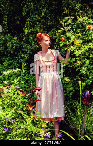 Jeune femme dans dirndl dans votre jardin et tient une rose jaune dans sa main. Banque D'Images