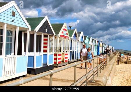 Southwold, Royaume-Uni. 12 juillet 2020. Les gens marchent devant les huttes de plage colorées de southwold.avec les plages en Angleterre maintenant entièrement ouvert avec seulement des mesures de distance sociales en vigueur, les gens prennent l'occasion de visiter certaines stations côtières. Southwold est une station balnéaire anglaise pleine de charme ancien et célèbre pour ses 300 cabanes de plage aux couleurs vives. Il y avait plein de gens à l'extérieur et sur la plage de sable et sur la jetée. Crédit : SOPA Images Limited/Alamy Live News Banque D'Images