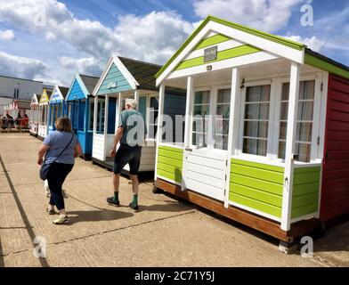 Southwold, Royaume-Uni. 12 juillet 2020. Un couple passe devant les huttes de plage colorées de southwold.avec les plages en Angleterre maintenant entièrement ouvert avec seulement des mesures de distance sociales en vigueur, les gens prennent l'occasion de visiter certaines stations côtières. Southwold est une station balnéaire anglaise pleine de charme ancien et célèbre pour ses 300 cabanes de plage aux couleurs vives. Il y avait plein de gens à l'extérieur et sur la plage de sable et sur la jetée. Crédit : SOPA Images Limited/Alamy Live News Banque D'Images