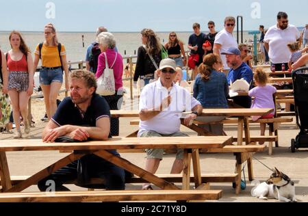 Southwold, Royaume-Uni. 12 juillet 2020. Les gens s'assoient à des tables et observent les distances sociales en attendant de prendre des boissons.avec les plages d'Angleterre désormais entièrement ouvertes avec seulement des mesures de distance sociales en vigueur, les gens prennent l'occasion de visiter certaines stations balnéaires. Southwold est une station balnéaire anglaise pleine de charme ancien et célèbre pour ses 300 cabanes de plage aux couleurs vives. Il y avait plein de gens à l'extérieur et sur la plage de sable et sur la jetée. Crédit : SOPA Images Limited/Alamy Live News Banque D'Images