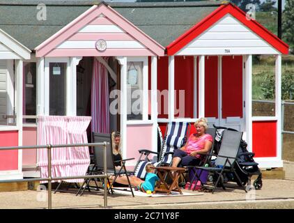 Southwold, Royaume-Uni. 12 juillet 2020. Les gens s'assoient à l'extérieur de leurs huttes pittoresques et colorées à Southwold.avec les plages en Angleterre maintenant entièrement ouvertes avec seulement des mesures de distance sociale en vigueur, les gens prennent l'occasion de visiter quelques stations côtières. Southwold est une station balnéaire anglaise pleine de charme ancien et célèbre pour ses 300 cabanes de plage aux couleurs vives. Il y avait plein de gens à l'extérieur et sur la plage de sable et sur la jetée. Crédit : SOPA Images Limited/Alamy Live News Banque D'Images