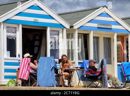 Southwold, Royaume-Uni. 12 juillet 2020. Les gens s'assoient à l'extérieur de leurs huttes pittoresques et colorées à Southwold.avec les plages en Angleterre maintenant entièrement ouvertes avec seulement des mesures de distance sociale en vigueur, les gens prennent l'occasion de visiter quelques stations côtières. Southwold est une station balnéaire anglaise pleine de charme ancien et célèbre pour ses 300 cabanes de plage aux couleurs vives. Il y avait plein de gens à l'extérieur et sur la plage de sable et sur la jetée. Crédit : SOPA Images Limited/Alamy Live News Banque D'Images