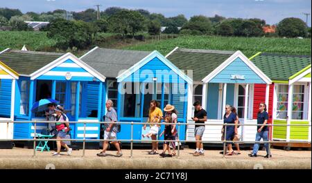 Southwold, Royaume-Uni. 12 juillet 2020. Les touristes marchent au-delà d'une ligne de huttes de plage colorées Southwold.avec les plages en Angleterre maintenant entièrement ouvert avec seulement des mesures de distance sociale en vigueur, les gens prennent l'occasion de visiter quelques stations côtières. Southwold est une station balnéaire anglaise pleine de charme ancien et célèbre pour ses 300 cabanes de plage aux couleurs vives. Il y avait plein de gens à l'extérieur et sur la plage de sable et sur la jetée. Crédit : SOPA Images Limited/Alamy Live News Banque D'Images