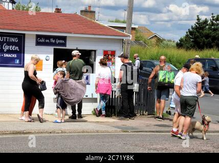 Southwold, Royaume-Uni. 12 juillet 2020. Les gens font la queue dans un café en bord de mer pour un service de plats à emporter.avec les plages d'Angleterre maintenant entièrement ouvertes avec seulement des mesures de distance sociales en vigueur, les gens prennent l'occasion de visiter certaines stations balnéaires. Southwold est une station balnéaire anglaise pleine de charme ancien et célèbre pour ses 300 cabanes de plage aux couleurs vives. Il y avait plein de gens à l'extérieur et sur la plage de sable et sur la jetée. Crédit : SOPA Images Limited/Alamy Live News Banque D'Images