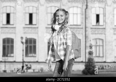 petite fille porte une chemise à carreaux. enfant avec casque au coucher du soleil. enfant printemps et mode d'été. enfance heureuse. e-learning avec ebook. technologie moderne. mélomane et sac à dos. Banque D'Images