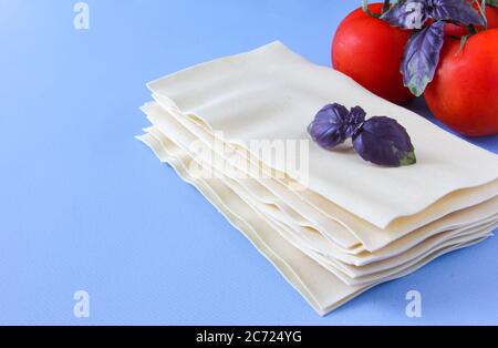 Feuilles de lasagne pâtes avec feuilles de tomate et de basilic sur fond bleu. Ingrédients pour une recette italienne. Copier l'espace. Banque D'Images