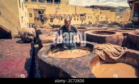 Fez, Maroc - avril 2018 : homme travaillant comme tanner dans les pots de teinture des tanneries de cuir vues de la terrasse de Tanneurs dans l'ancienne médina Banque D'Images