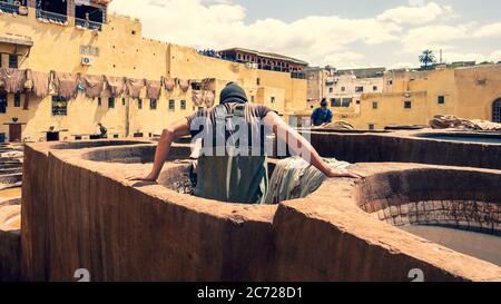 Fez, Maroc - avril 2018 : homme travaillant comme tanner dans les pots de teinture des tanneries de cuir vues de la terrasse de Tanneurs dans l'ancienne médina Banque D'Images