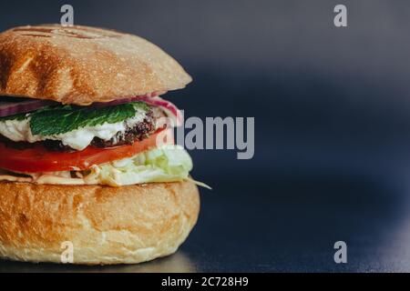 Circulaire Burger. Hamburger au fromage avec viande grillée, fromage, salade et rondelles d'oignon. Gros plan de délicieux hamburgers maison frais sur fond bleu écorce Banque D'Images