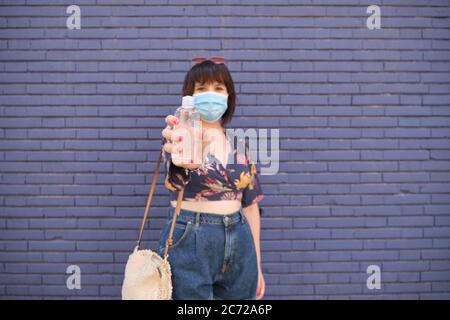 Jeune femme caucasienne portant un masque facial et montrant du gel désinfectant sur l'appareil photo. Concept de prévention des coronavirus. Banque D'Images