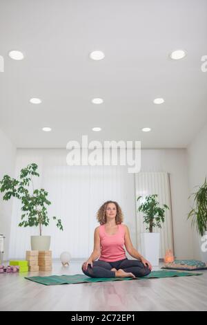 une jeune femme d'âge moyen pratiquant le yoga, à l'intérieur dans un studio de yoga, assise sur un tapis de yoga, souriant, regardant l'appareil photo. Banque D'Images