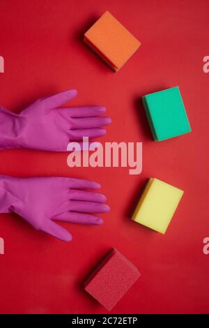 Vue à grand angle des gants en caoutchouc et des éponges colorées isolées sur fond rouge Banque D'Images