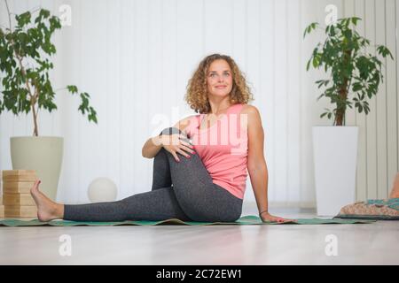 une jeune femme d'âge moyen pratiquant le yoga, à l'intérieur dans un studio de yoga, en s'étirant sur le côté assis. Banque D'Images