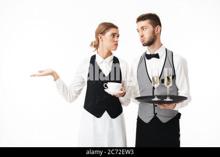 Un jeune serveur tient un plateau avec des verres de champagne et une serveuse triste tenant une tasse de café entre les mains, regardant tiredly l'un sur le dos blanc Banque D'Images