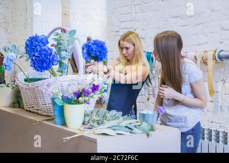 Deux artistes fleuristes professionnels, fleuristes en train de réaliser un grand panier floral avec des fleurs à l'atelier, fleuriste. Fleuriste, fait main, mariage Banque D'Images