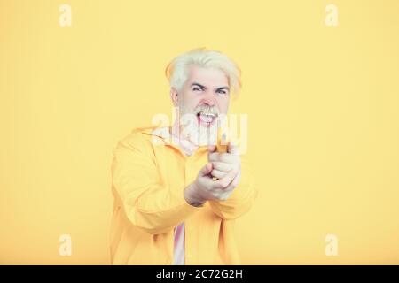 Portrait de drôle jeune homme debout sur fond jaune et utilisant la banane comme arme, regardant l'appareil photo avec le visage sérieux et jouant l'espion Banque D'Images